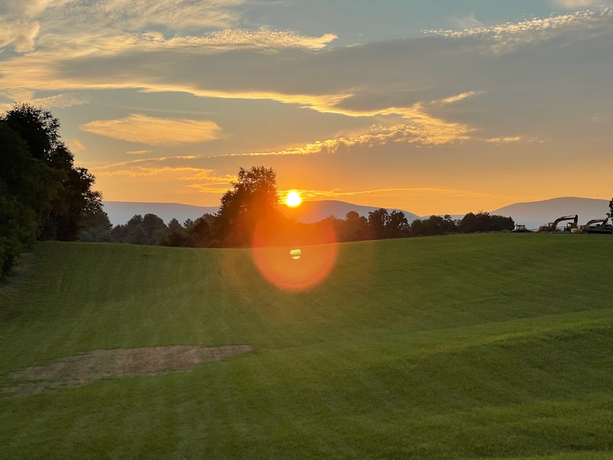 Sunset over open fields, the sun a small bright disc above the tree line