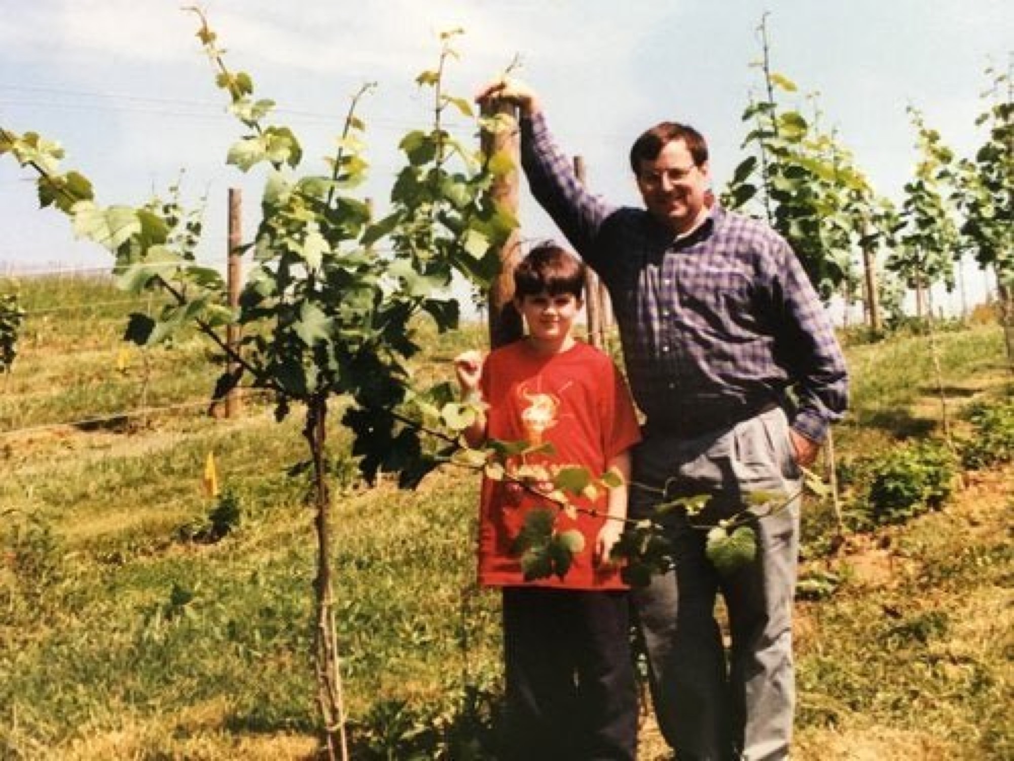 A man and woman in a row of young vines, holding tools and smiling